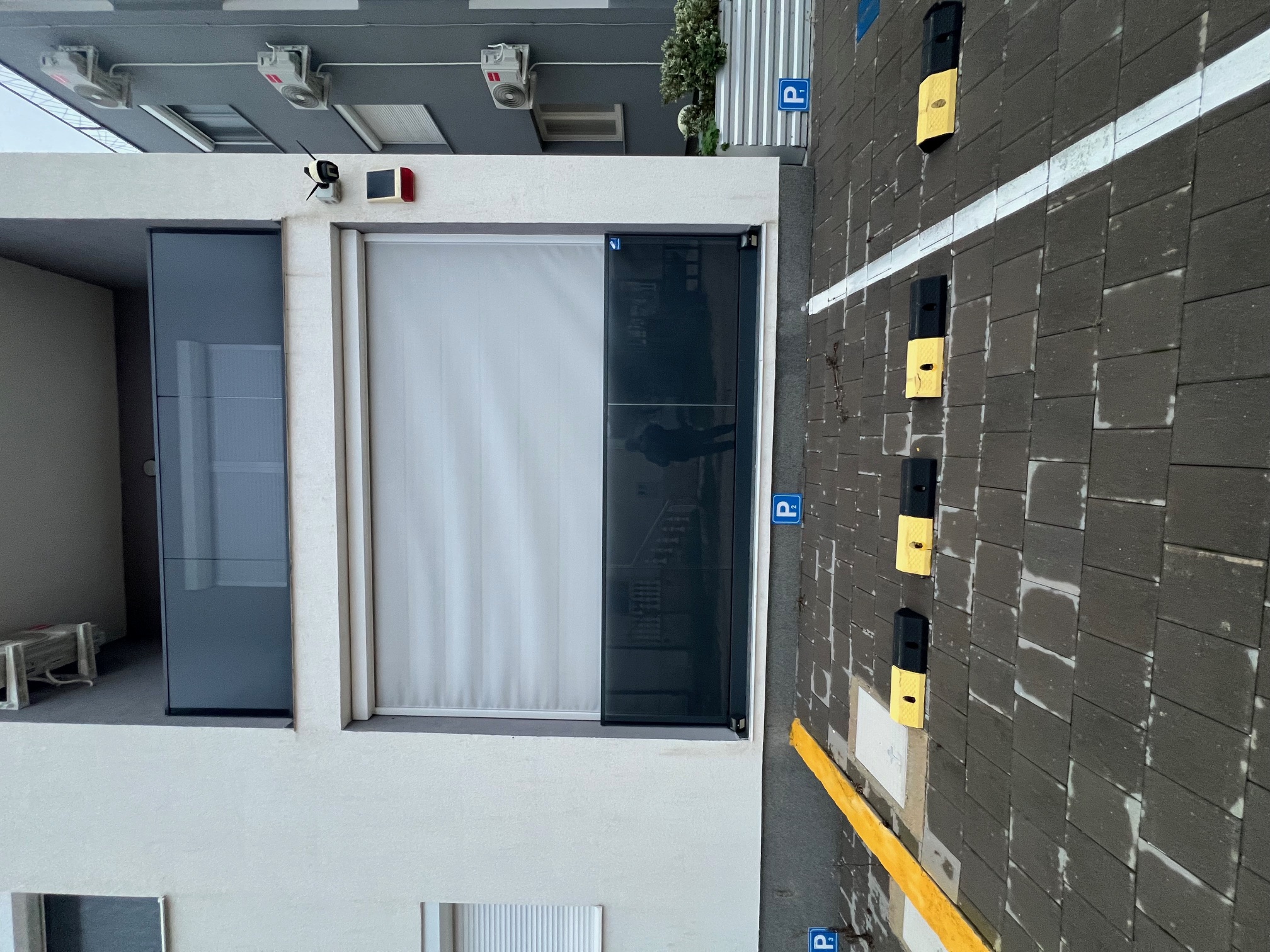 Épület homlokzata térkövezett parkolóval